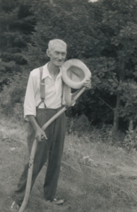 Older man holding a hat and scythe