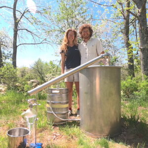 two farmers stand behind a large metal still used for distilling