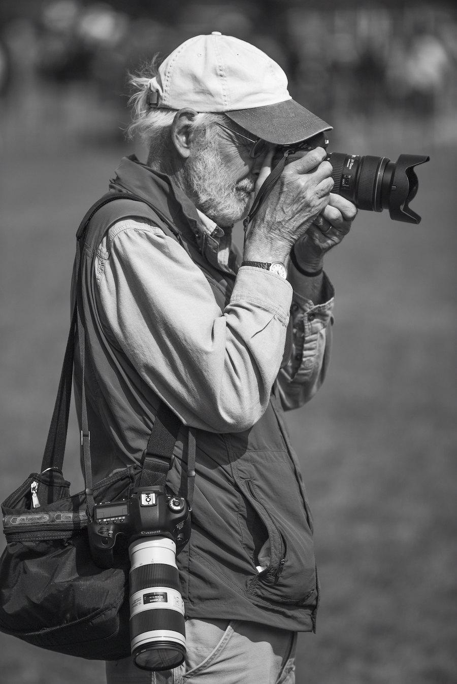 Photographer squinting into a camera with an extended lens; another camera dangles from their side