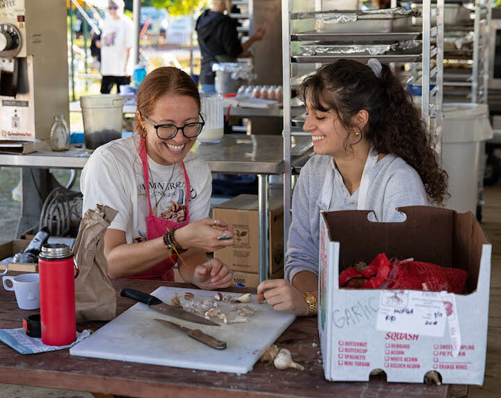 two volunteers in aprons chop garlic