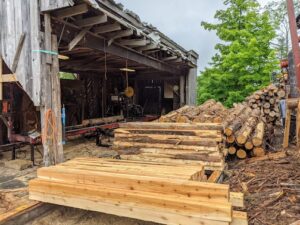 stacks of cedar logs and lumber next to a three-sided building