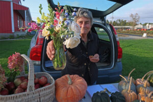 a farmers' market vendor holds out a bouquet of mixed flowers in a glass vase