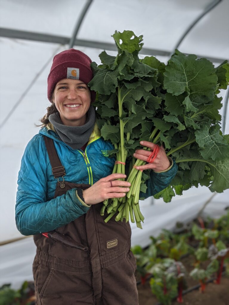 A farmer holds an armful of greens in a greenhouse.