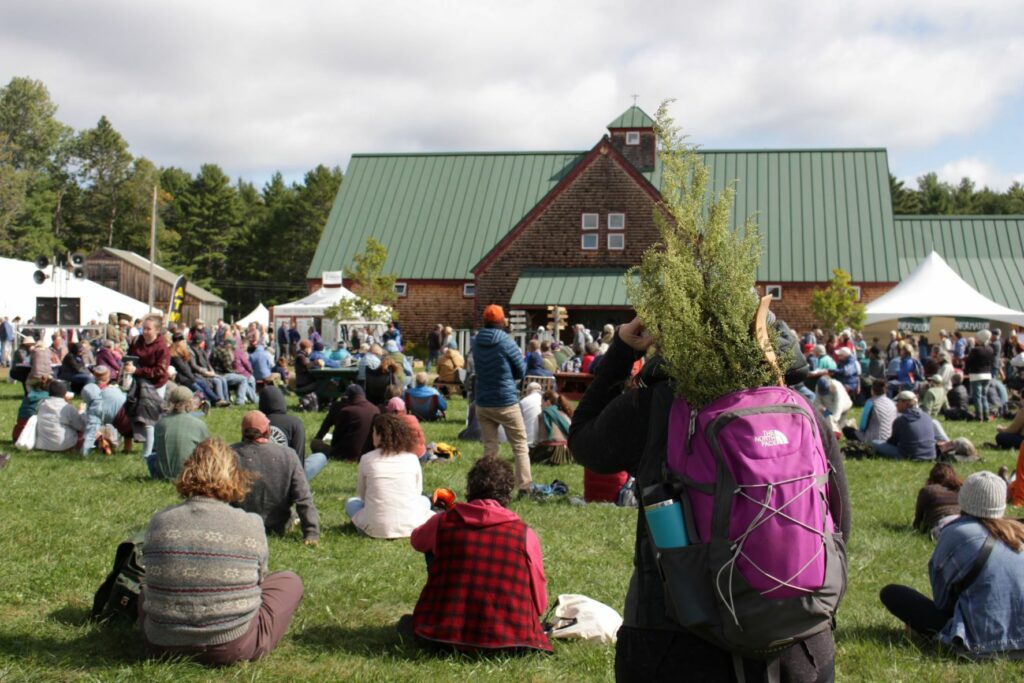 A fairgoer stands with a backpack full of sweet Annie watching a keynote speech at the Common Ground Country Fair.