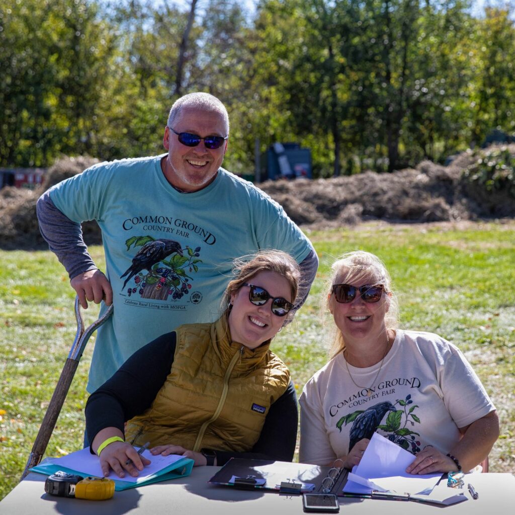 Three people sitting at a table near a manure pile.