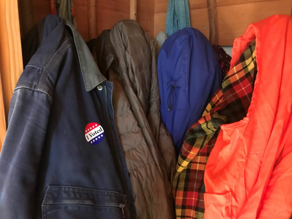 Winter coats hung up on pegs, one with a sticker that says "I Voted."