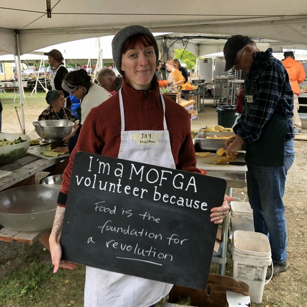 A MOFGA volunteer holds a sign that says "Food is the foundation for a revolution."