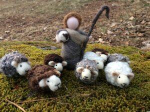 Felted wool sheep on a background of moss with a felted shepherd holding a baby lamb.