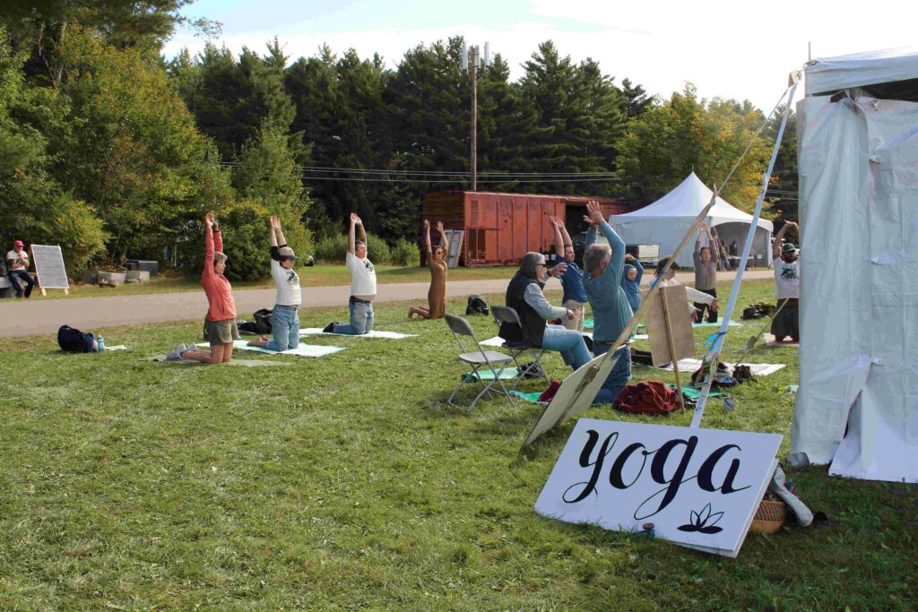 Participants stretch upward in a yoga pose at an outdoor class.