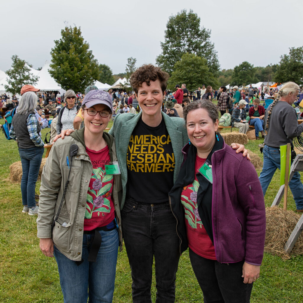 Three people pose in front of the packed common at the Common Ground Country Fair.