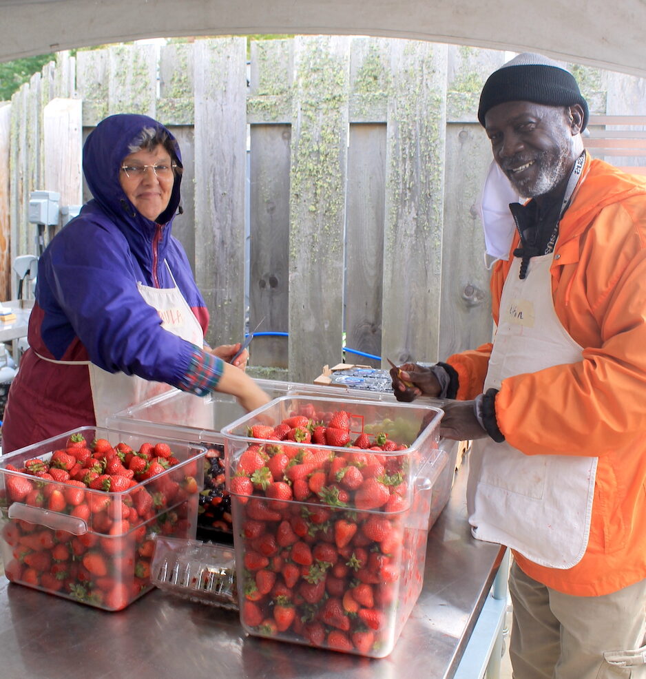 Two volunteers cutting strawberries in the Common Kitchen.