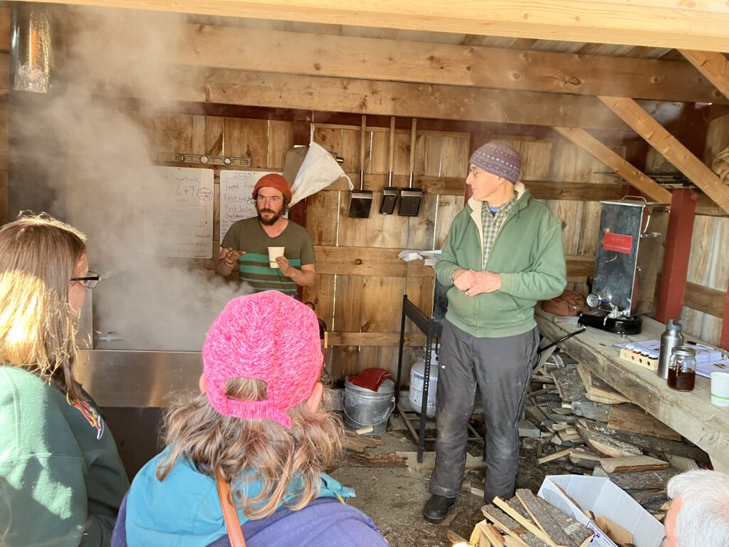 Two instructors discuss the operations of a sugarhouse to a group of tour participants.