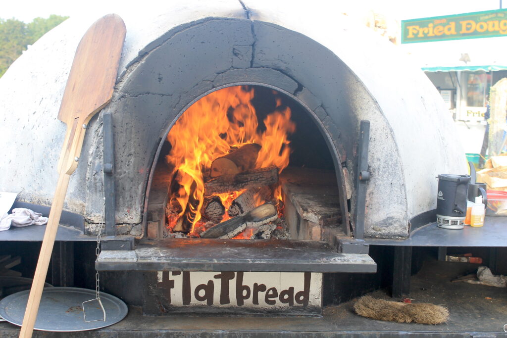 A wood-fired oven, with a sign reading "flatbread" cooks pizzas