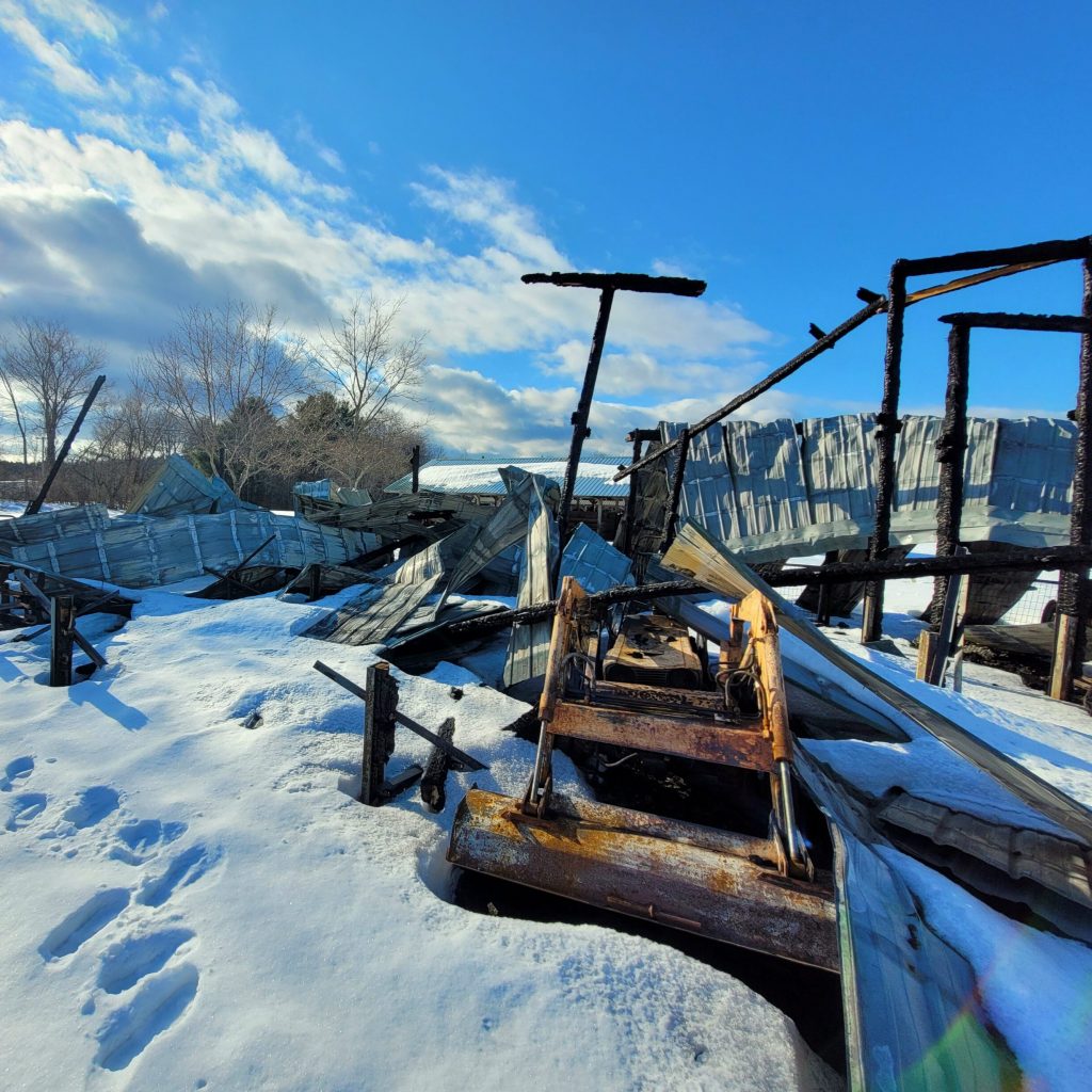 A ruined tractor in the debris of a barn fire.