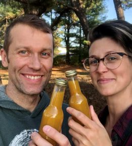 Two people smiling holding up bottles of orange hot sauce.