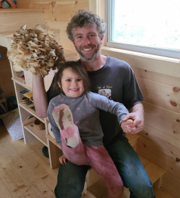 farmer smiling, holding mushrooms and child