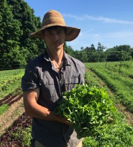 Farmer in straw hat holding lettuce.