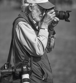 Photographer squinting into a camera with an extended lens; another camera dangles from their side