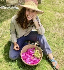 A farmer poses in front of a basket of rose petals.