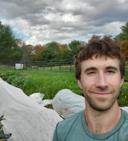 A farmer smiling in front of covered crop rows and kale.