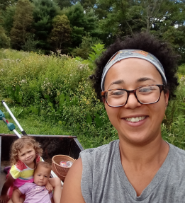 A farmer smiling with a wagon with two children behind them.