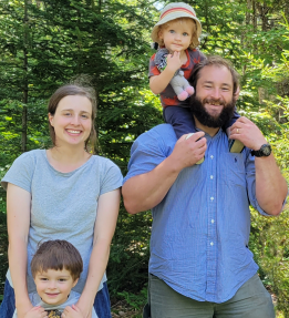 Two farmers posing with their two children in front of a forest.