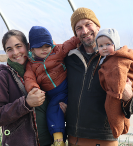 Two farmers pose with their two children in a green house.