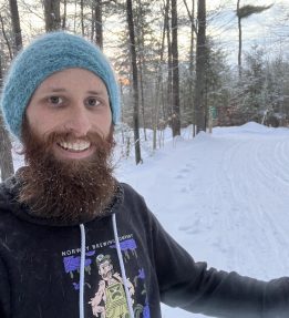 MOFGA Volunteer Daniel Sipe stands in the snow-covered woods.