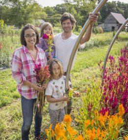 A family of four standing near a high tunnel of celosia flowers on their farm.